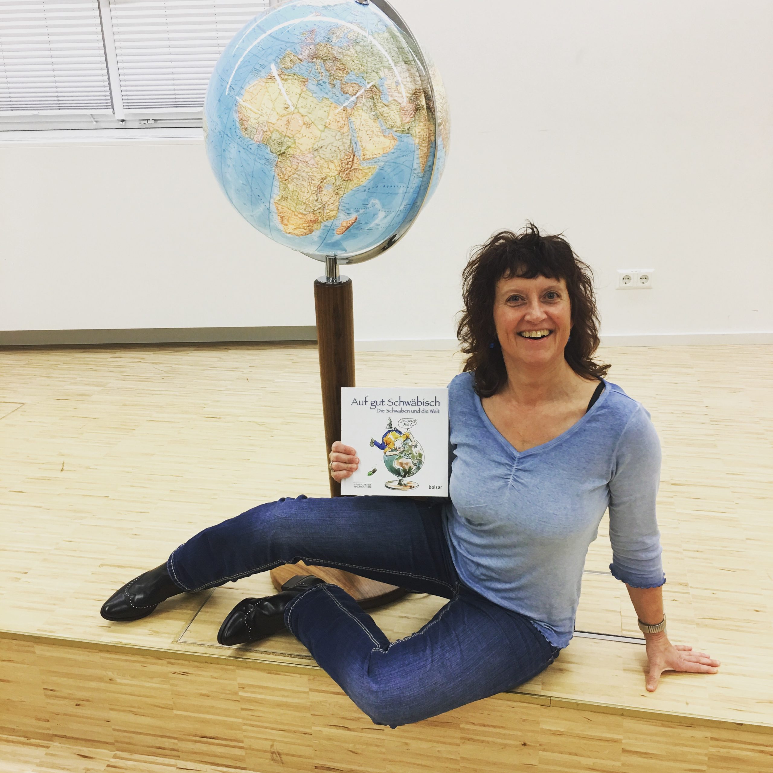 Marion Kinzig sitzt vor einem Globus und präsentiert das Buch ‚Auf gut Schwäbisch – Die Schwaben in der Welt‘.