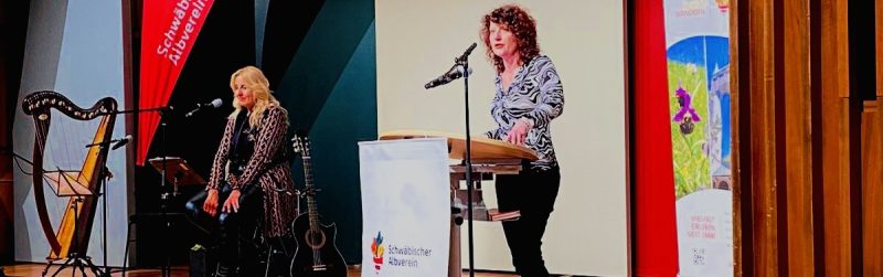 Marion Kinzigliest beim Mundartfestival des Schwäbischen Albvereins – Musikerin Claudia Pohel im Hintergrund